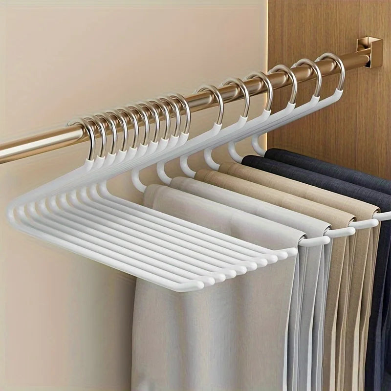 Les cintres blancs dans un dressing, pantalons beiges, gris et bleu marine côte à côte