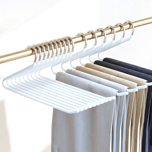 Dix cintres en Z blancs alignés sur une tringle dorée, chacun portant un pantalon plié en deux