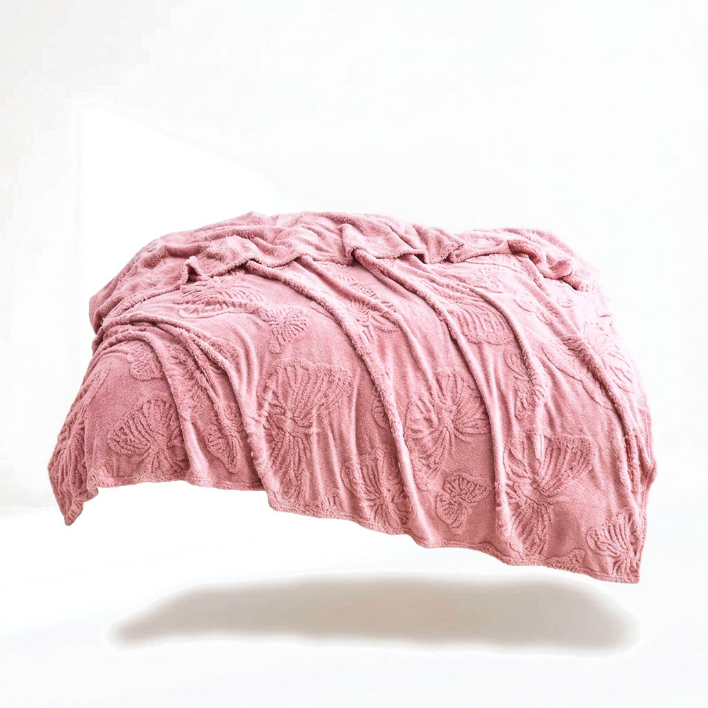 Le plaid rose poudré drapé sur fond blanc, motif de papillons tissé en relief